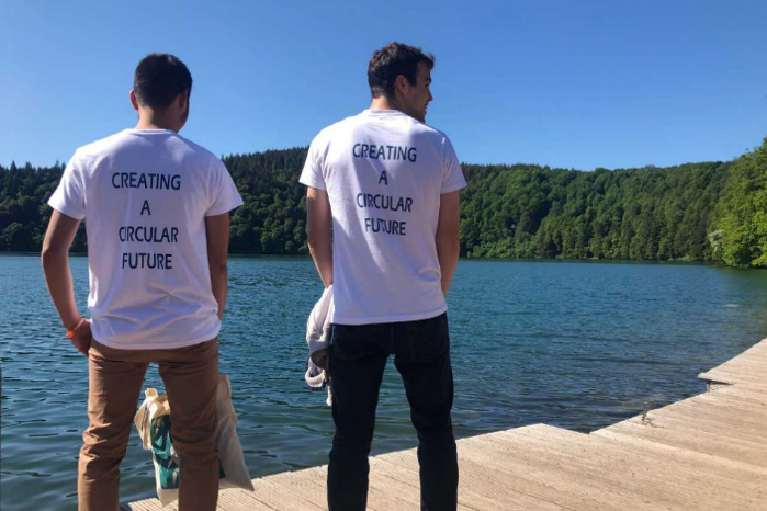 Two men standing at the border of a lake, wearing t-shirts saying Creating a Circular Future