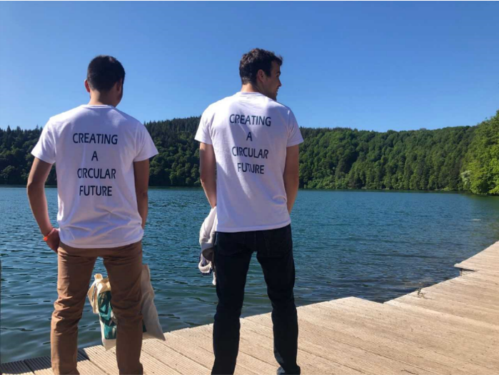 Two men standing at the border of a lake, wearing t-shirts saying Creating a Circular Future