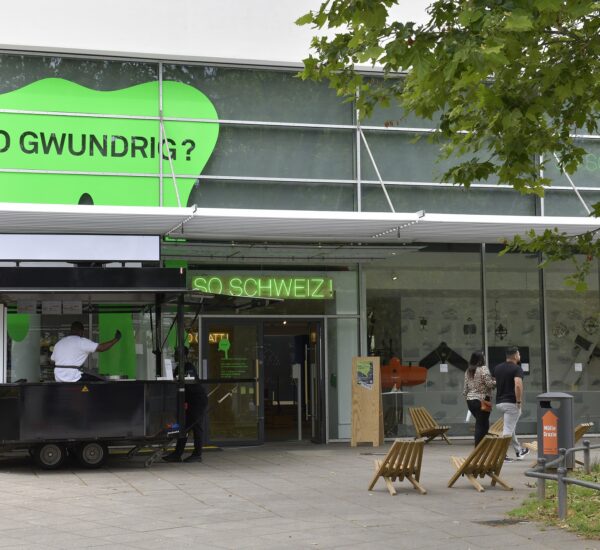 The entrance of a modern house with a green sign above saying "so gwundrig"