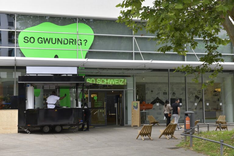 The entrance of a modern house with a green sign above saying "so gwundrig"